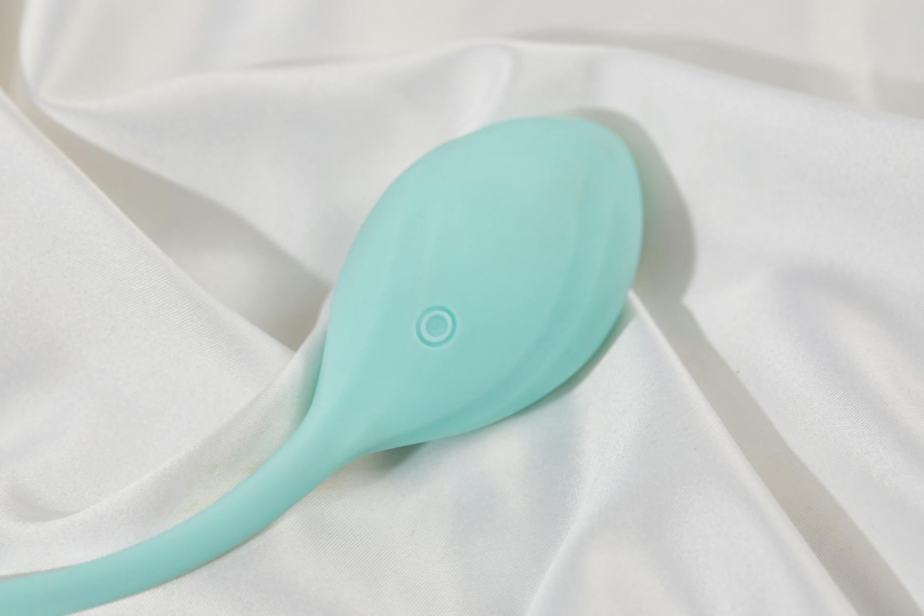 A sleek teal clitoral vibrator resting on soft white fabric, ready for comfortable use