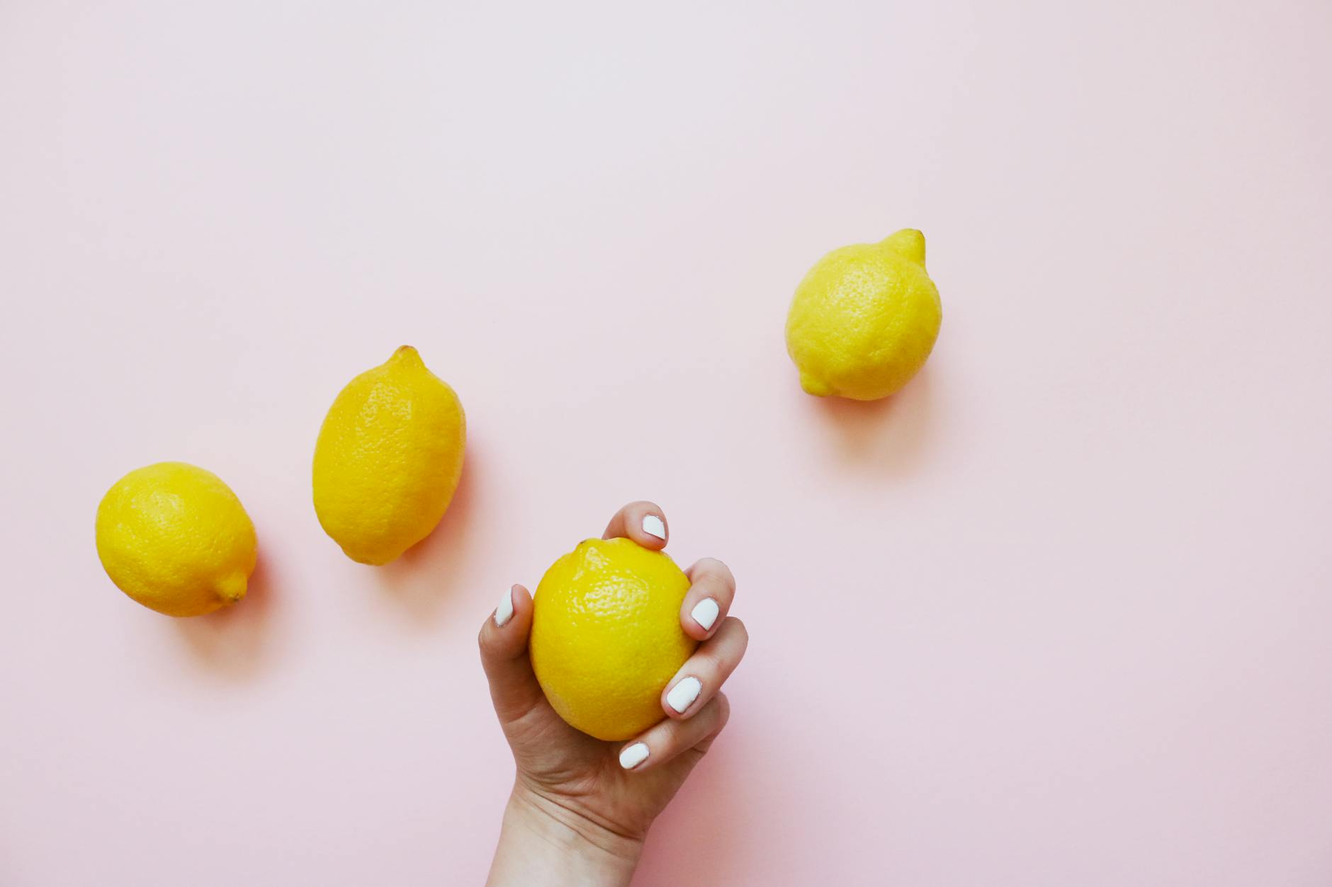 A hand holding a lemon on a soft pink background, symbolizing fresh beginnings and vulnerability
