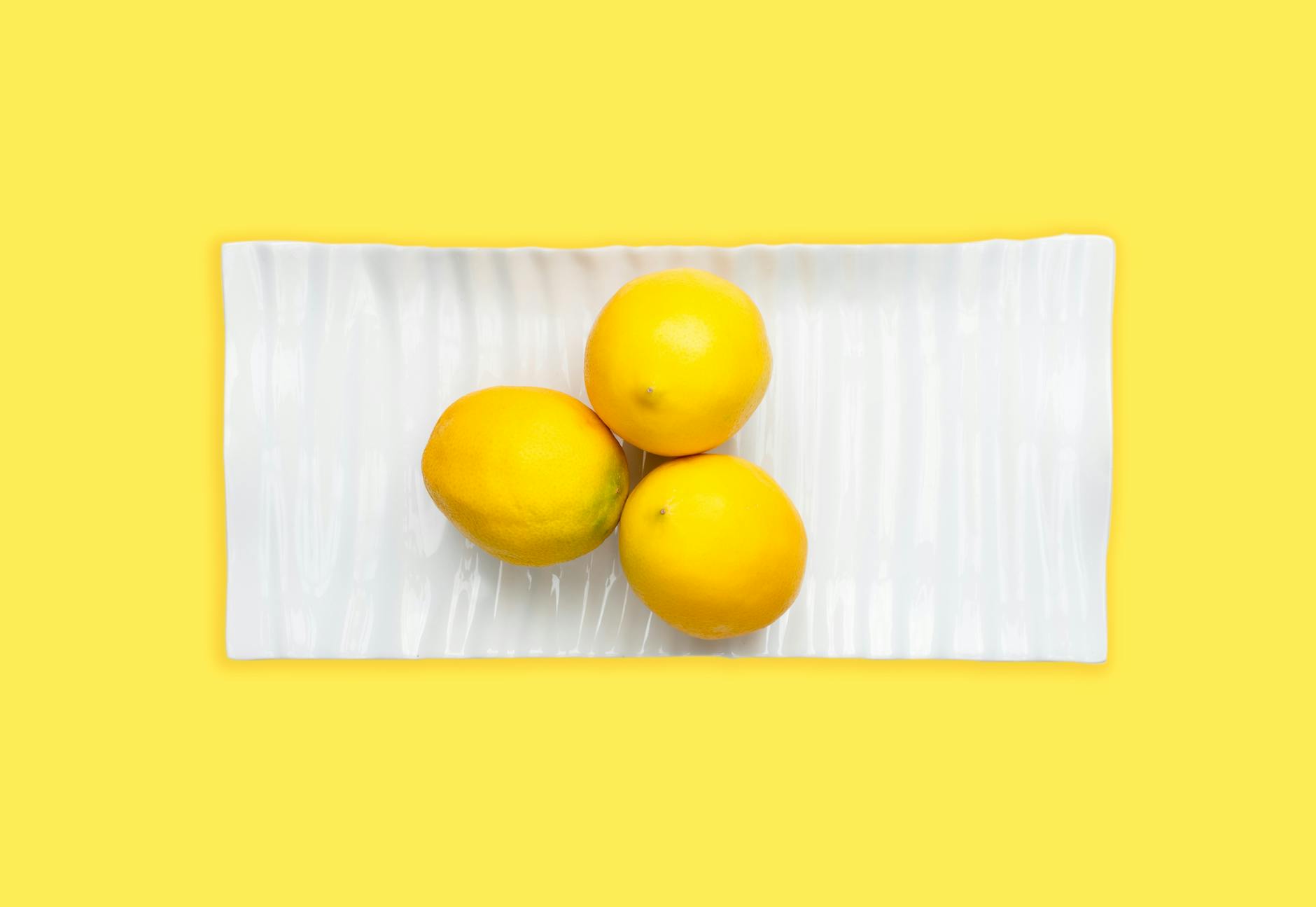 Fresh lemons arranged on a white plate with yellow background