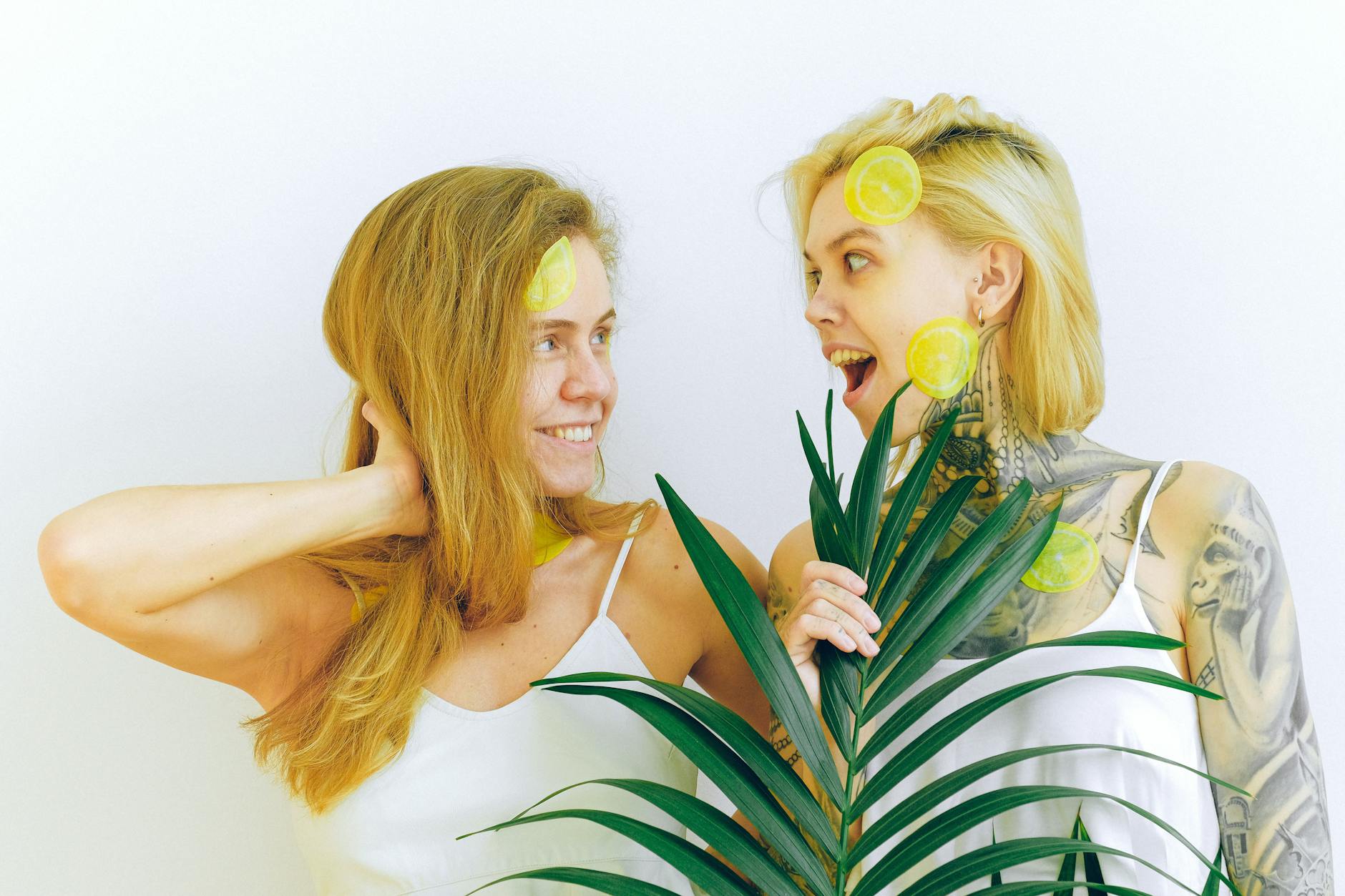 Two women smiling and expressing joy while holding fresh lemons together indoors