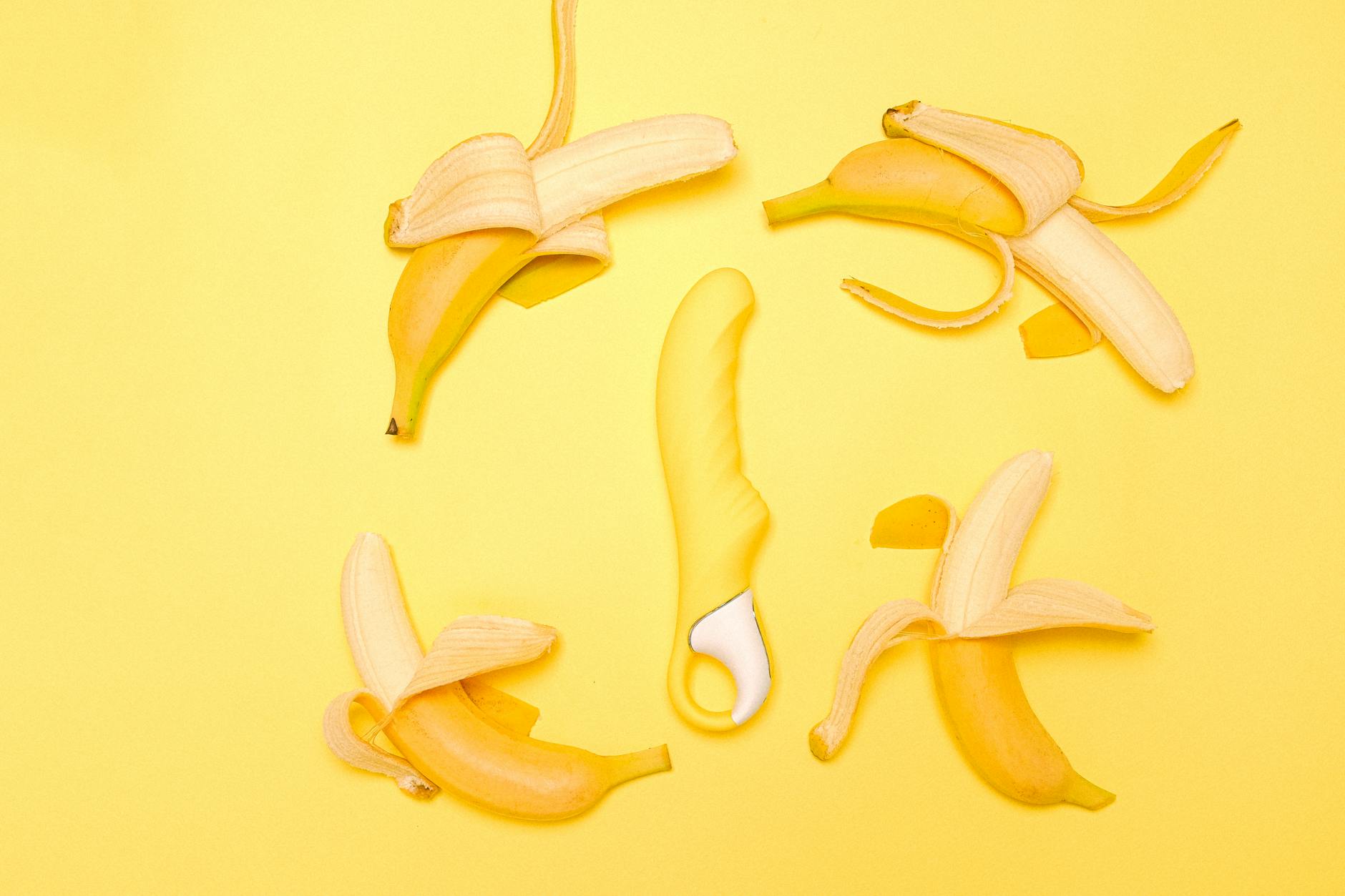 Yellow silicone lemon vibrator surrounded by fresh lemons on a warm yellow background.
