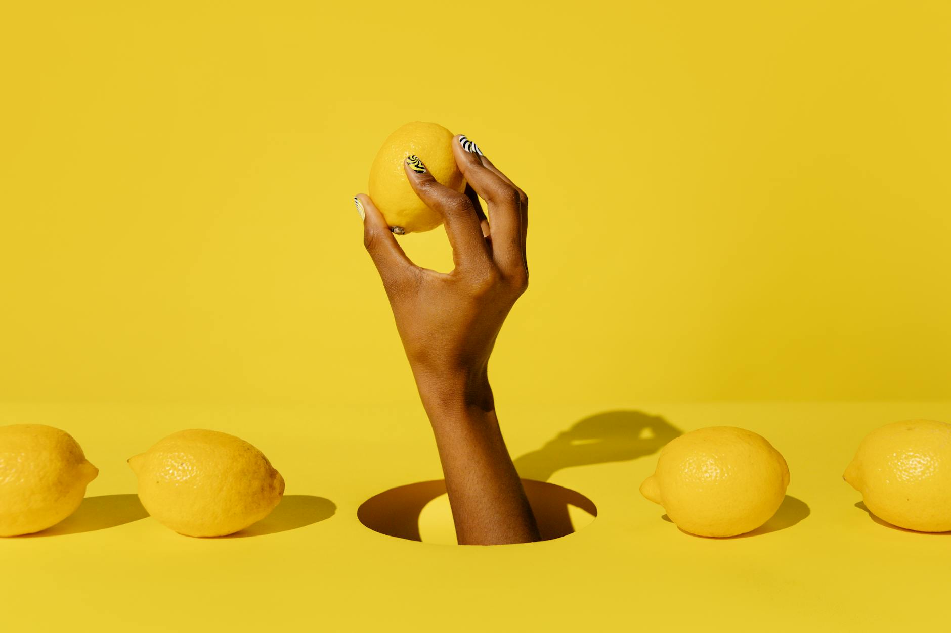 Hand holding a fresh lemon against a bright yellow background, representing citrus energy and renewal