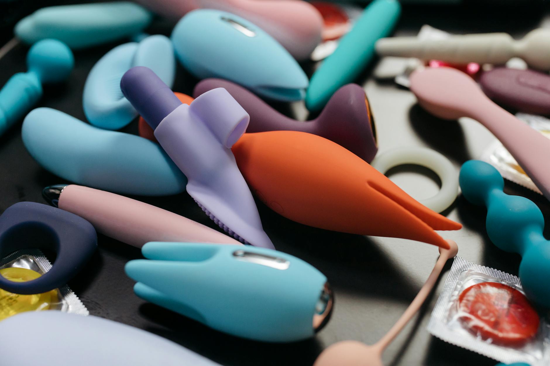 Person holding blue and pink silicone vibrators with thoughtful expression