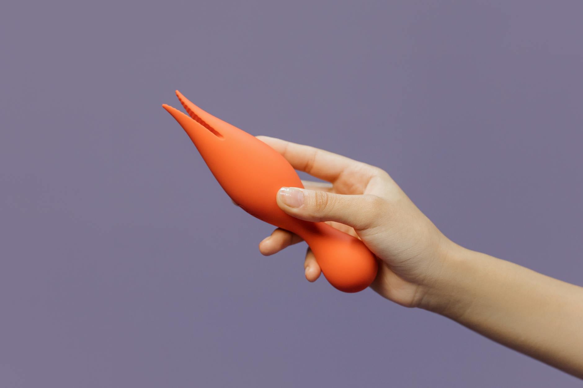 Close-up of a person's hand holding a lemon clitoral vibrator against a minimalist purple backdrop