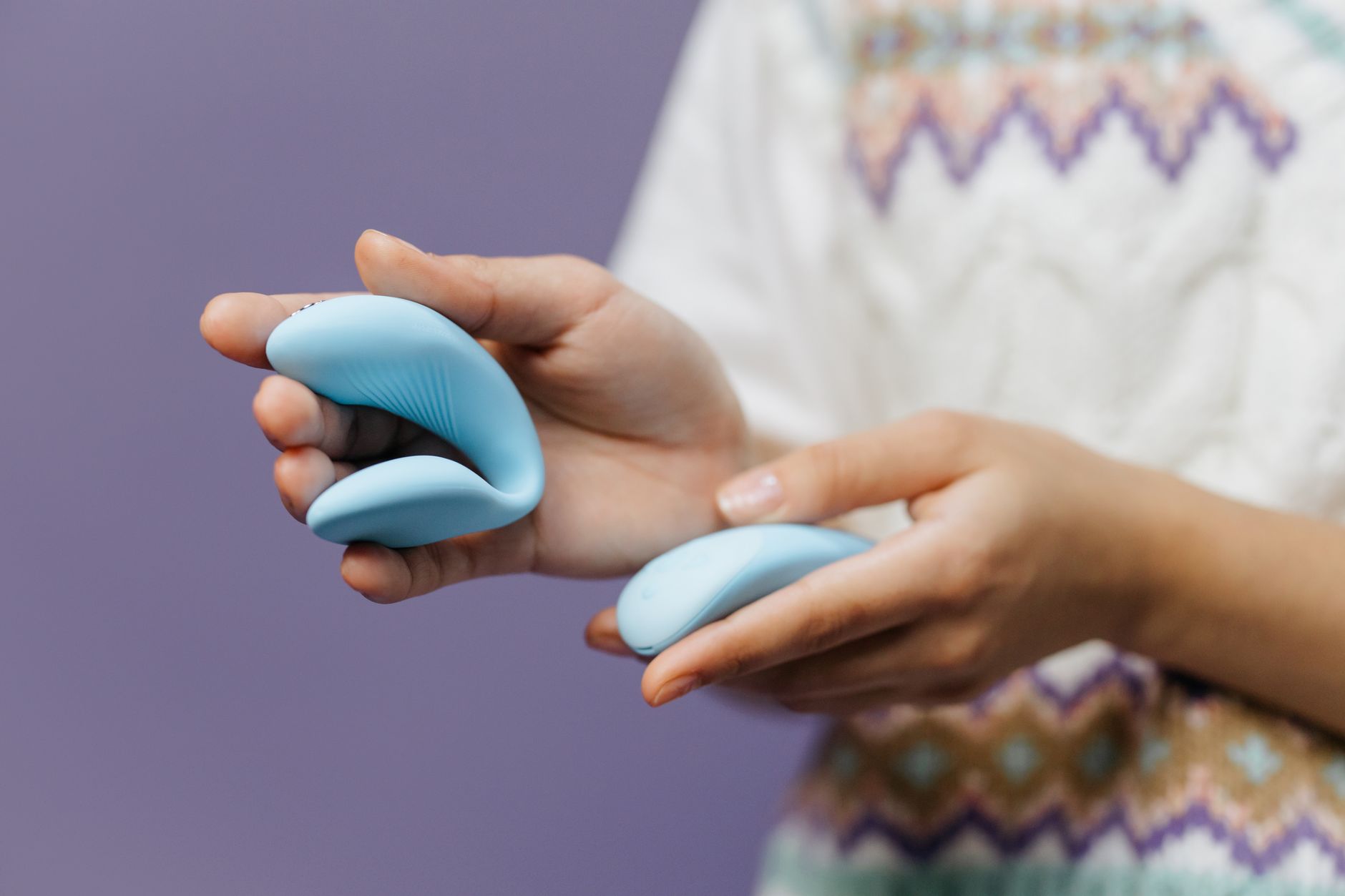 Intimate close-up of hands holding a sleek blue vibrator against a purple background