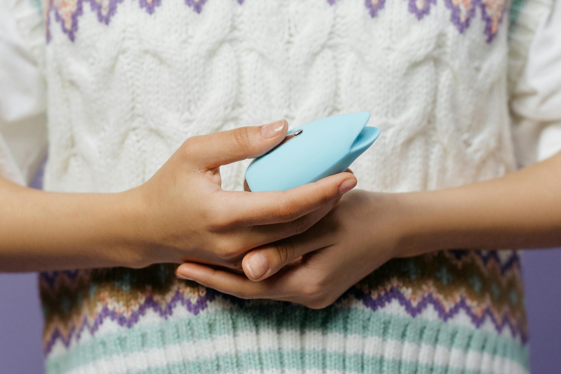 Woman with eyeglasses holding blue and pink silicone vibrators in a contemplative manner.